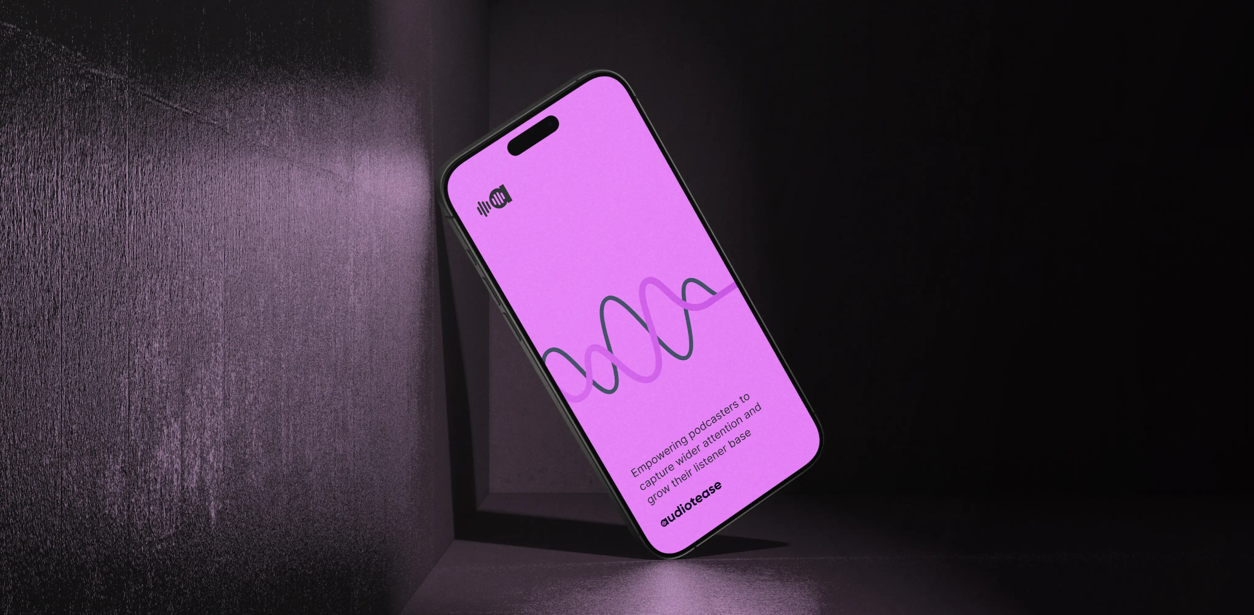 A smartphone displaying the Audiotease app screen with a purple background. The screen shows a wave design, the Audiotease logo, and the text 'Empowering podcasters to capture wider attention and grow their listener base.' The phone is set against a dark background with subtle lighting.