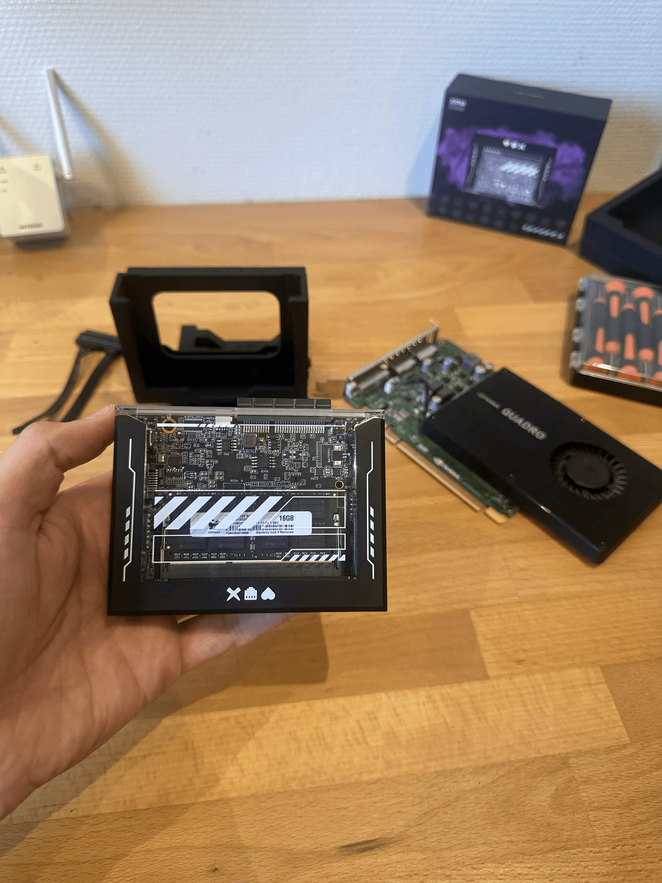  Hand holding a ZimaBlade 7700 with visible 16GB RAM, with an NVIDIA Quadro K2200 lying on the desk behind it.