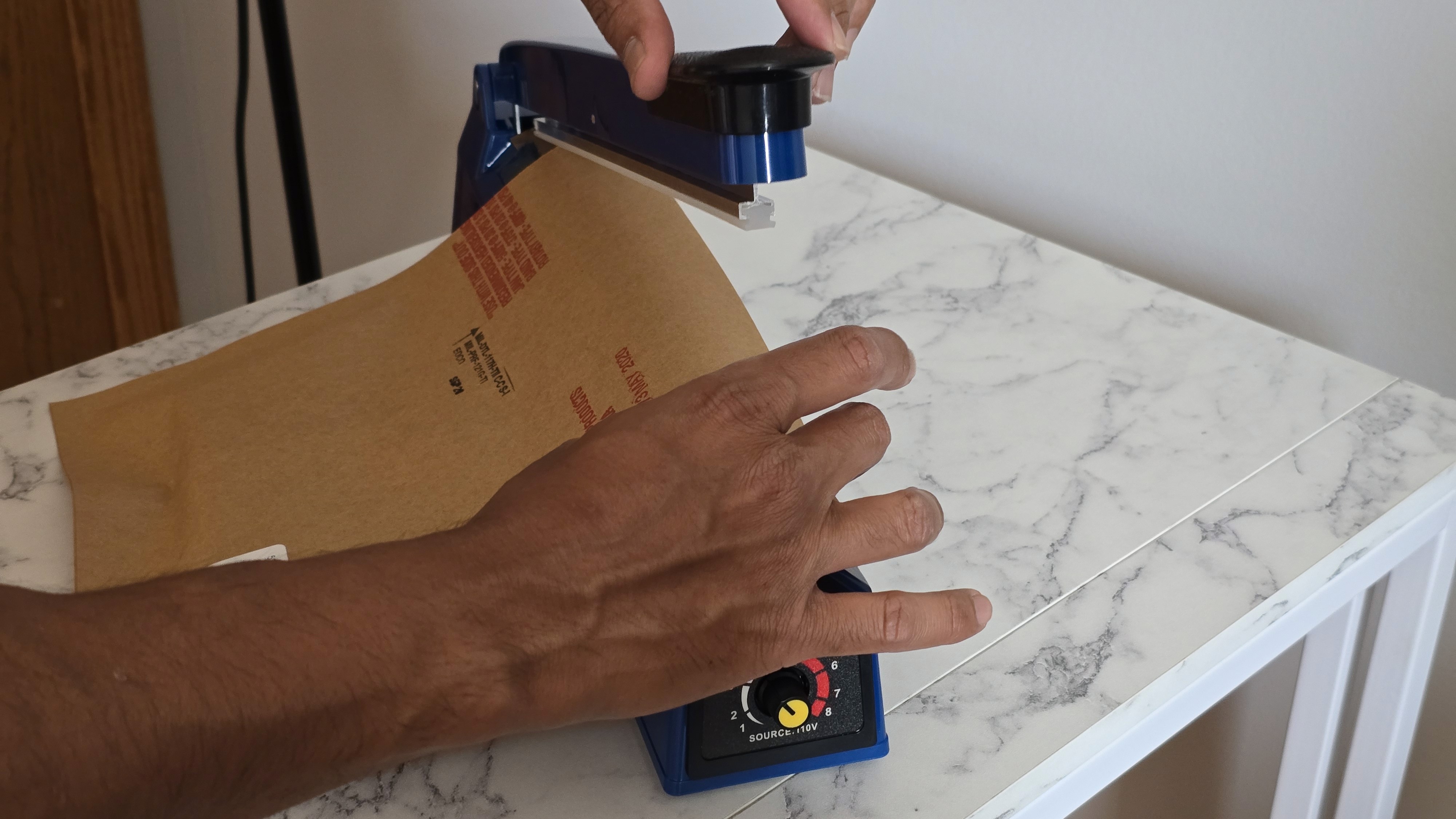 A young person with curly hair smiles at the camera while sitting in front of a laptop against a dark background.