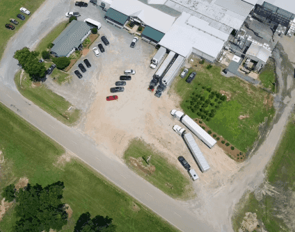 Aerial photo of a company parking lot with cars and warehouses, where three trucks are parked in reverse, with their rear ends inserted into the warehouse