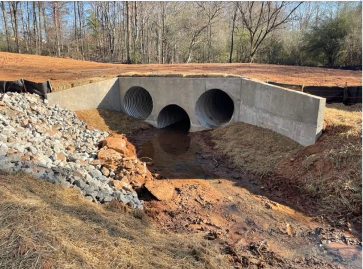 Triple culvert installation with concrete headwalls and riprap outlet protection on a graded drainage channel.