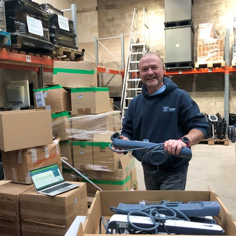 Photo of a Turing Trust volunteer working in the wharehouse surrounded by inventory