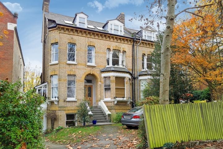A smiling man with curly hair is sitting at a desk, looking at the camera, with a laptop and a lamp in the background.