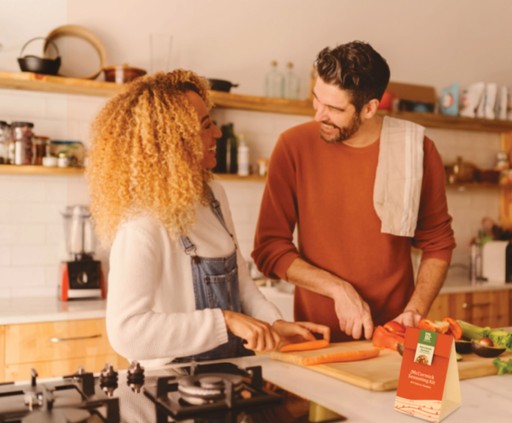 Younger couple cooking together, chopping vegetables.