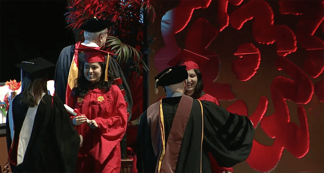 A photo of a couple of grad students and teachers, dressed in SVA color robes, that are hugging and congratulating each other.