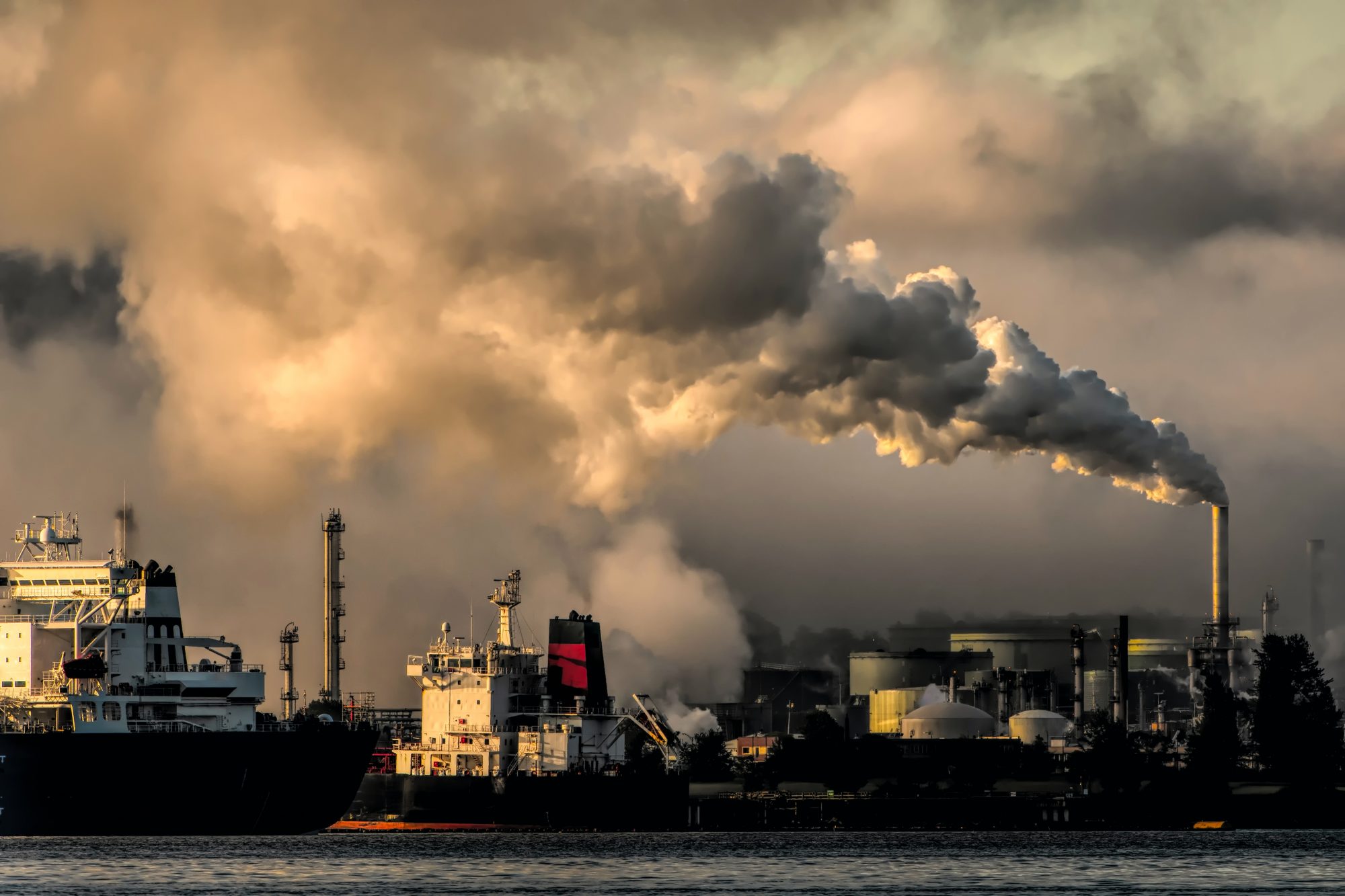 Industrial landscape with smokestacks emitting emissions, under a cloudy sky, highlighting pollution concerns.