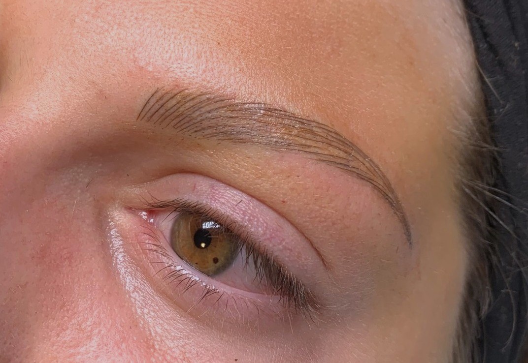 Close-up of freshly microbladed eyebrows with fine, natural-looking strokes. The skin appears slightly red from the procedure.