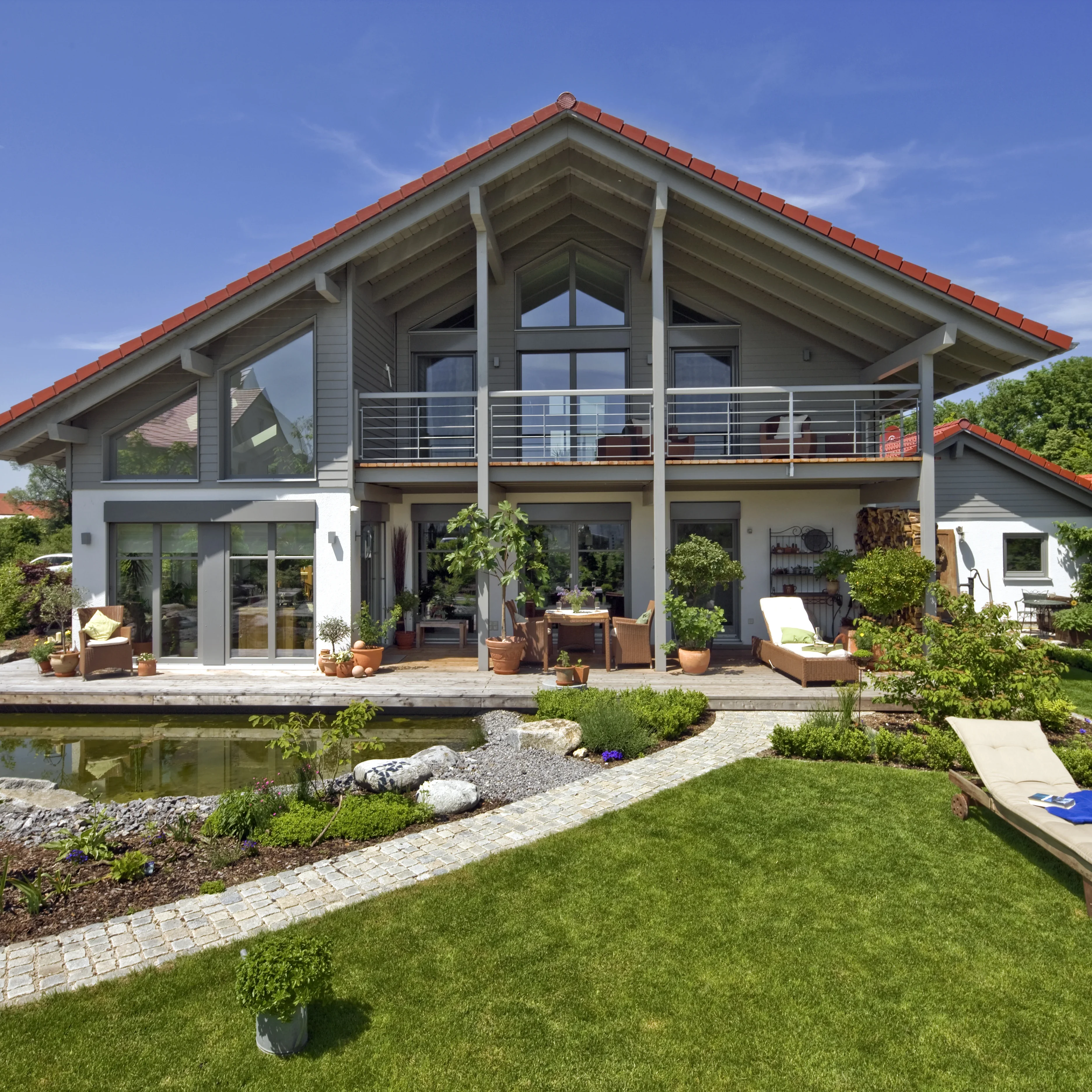 Modernes Einfamilienhaus mit großem Garten, Teich und Terrasse, unter blauem Himmel.