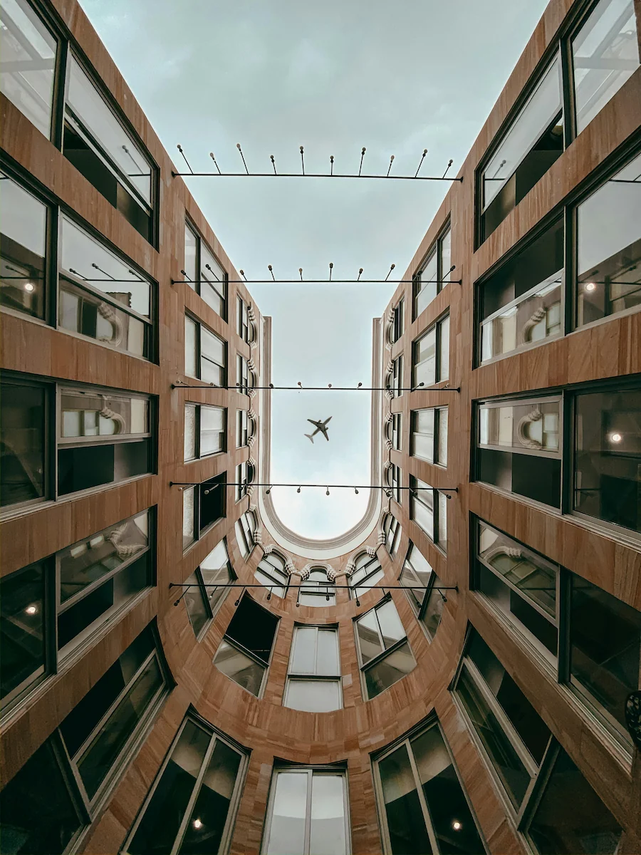 Modern courtyard buildings in Dammam, Saudi Arabia, viewed from below with an airplane overhead.