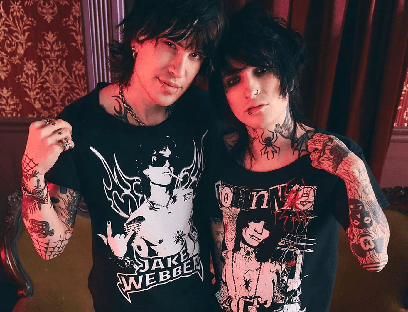 Tattooed couple in graphic band tees from Hot Topic posed against dark patterned wallpaper