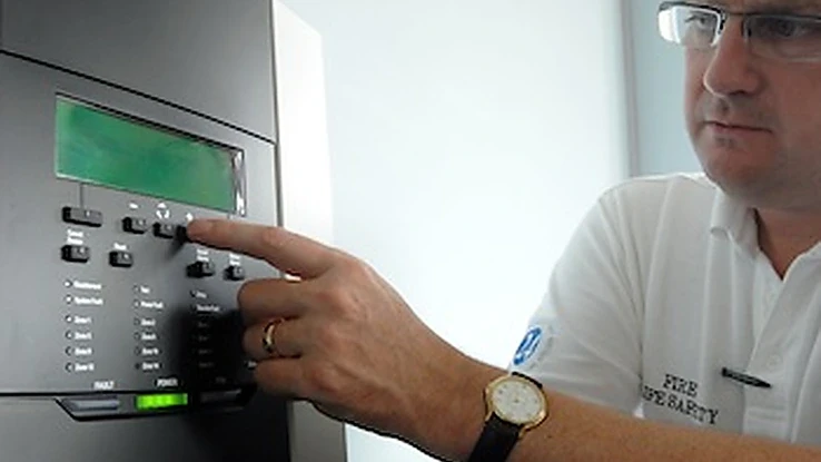 Fire safety engineer operating a fire alarm control panel during system testing.