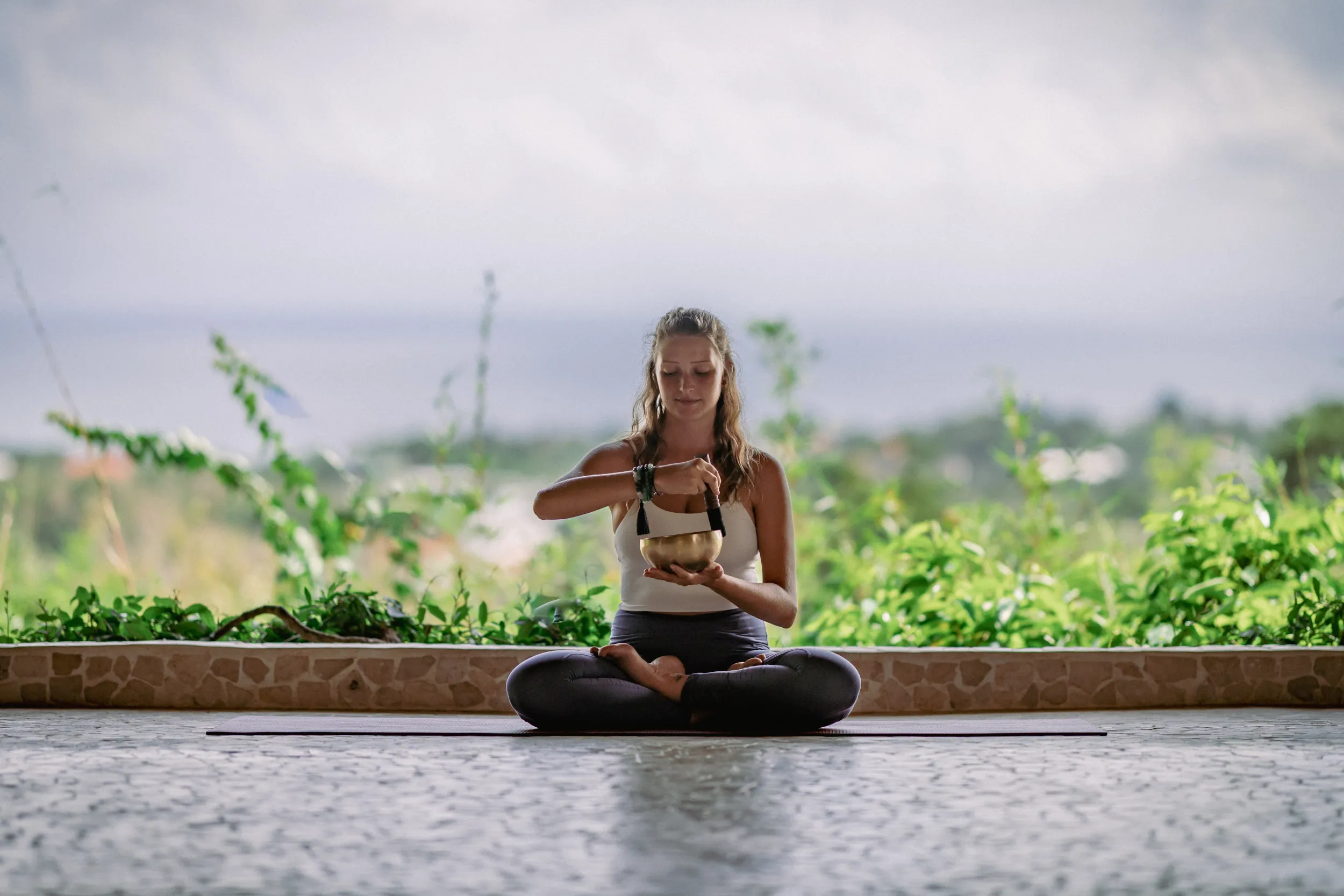 Two students practicing partner meditation in the bamboo yoga shala with a large Buddha painting background.