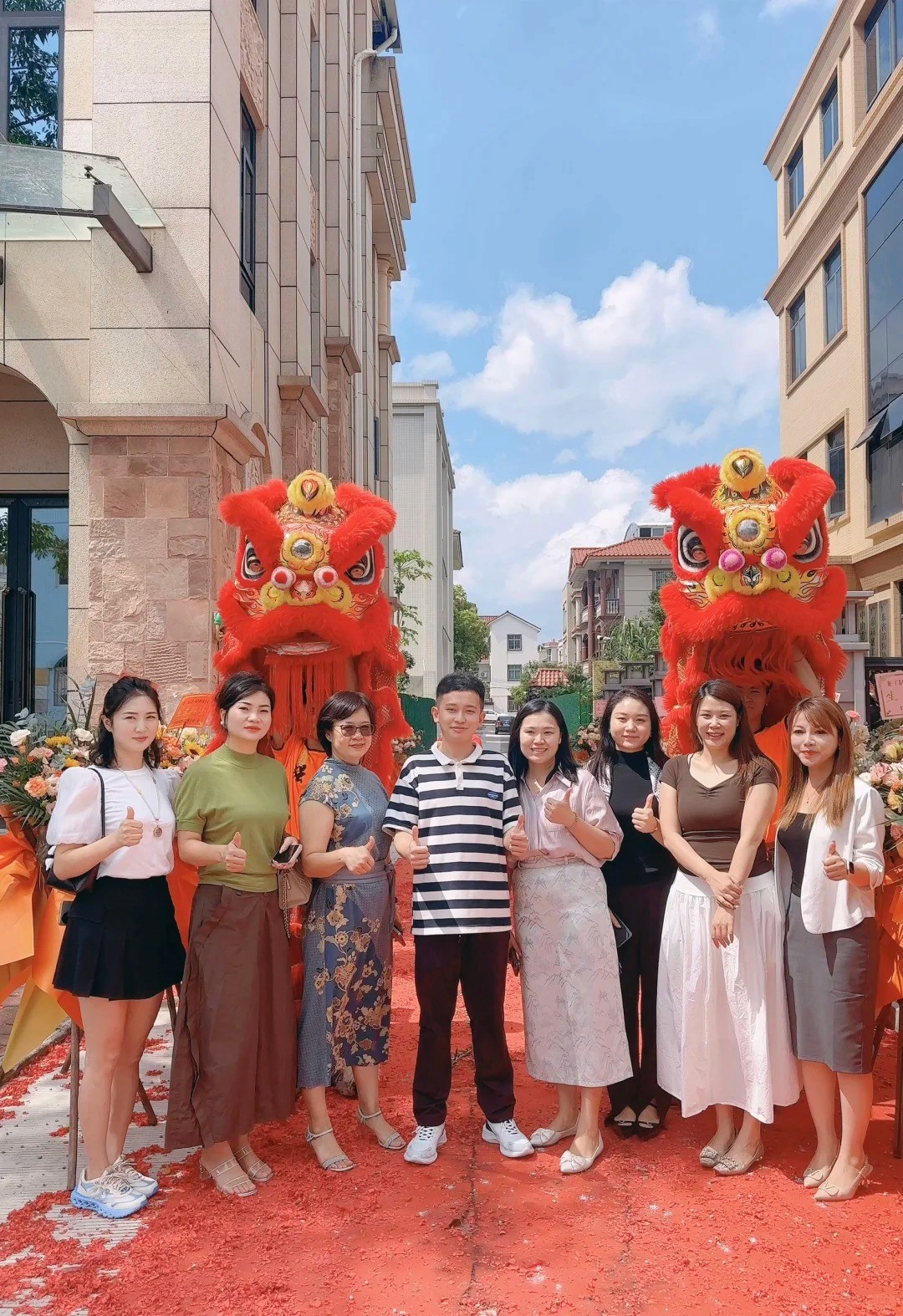 公司開張醒獅慶祝現場，公司團隊站在兩頭紅色醒獅前合照，象徵開業大吉與生意興隆 Group photo of company team standing in front of two red lion dance figures at a grand opening ceremony, celebrating a prosperous business start with traditional blessings