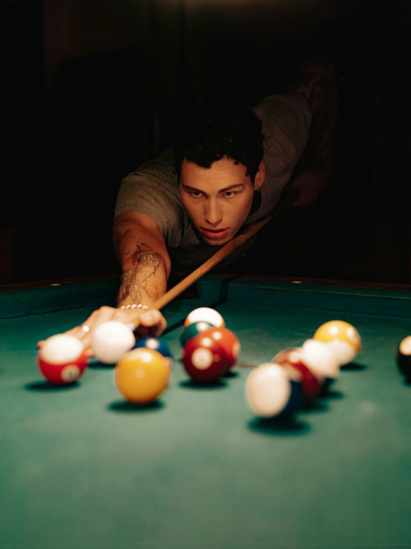 Person konzentriert beim Billardspiel, zielt mit Queue auf Kugeln auf grünem Tisch, dramatisches Licht.