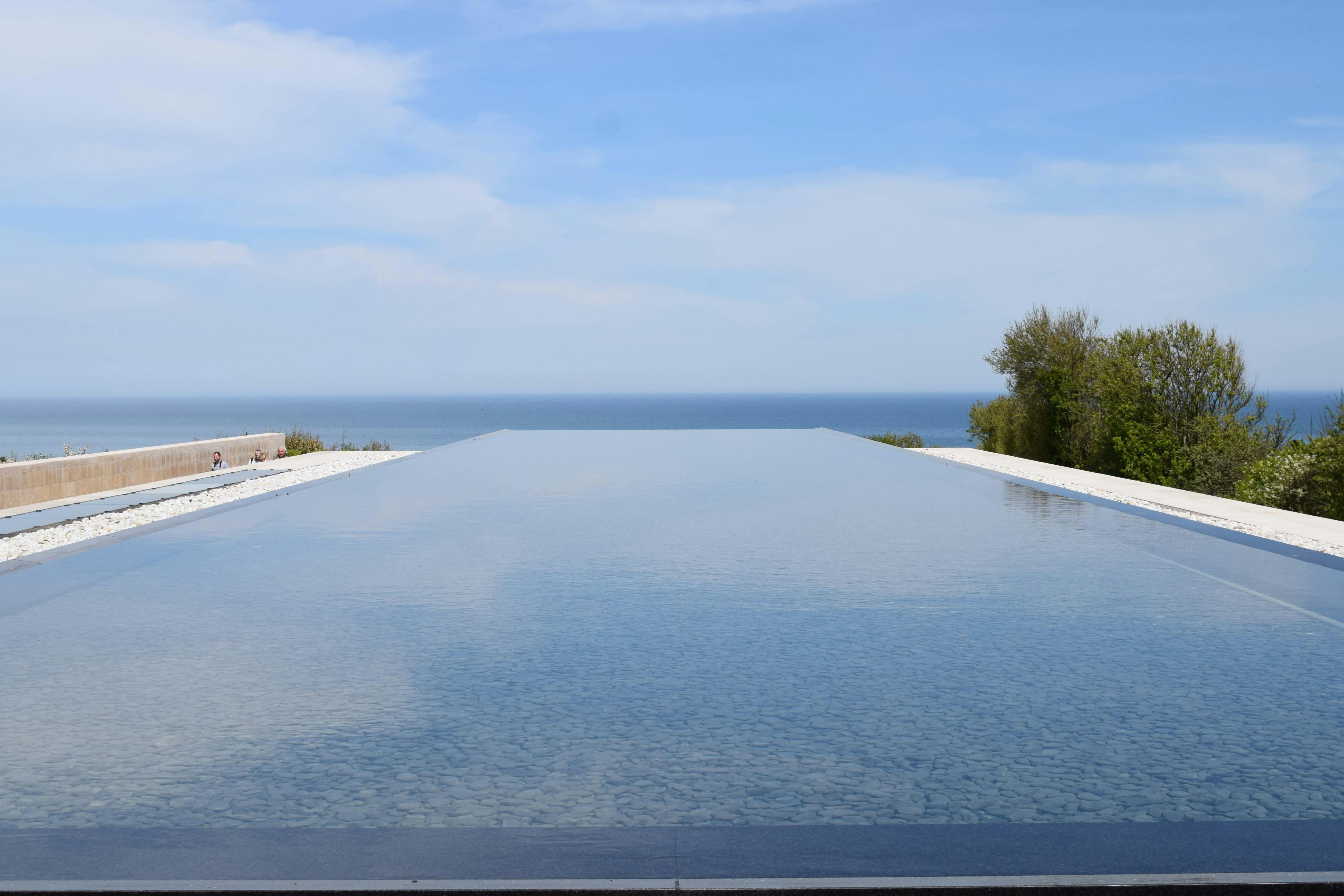 Infinity pool with a calm, reflective surface overlooking the sea under a bright blue sky.