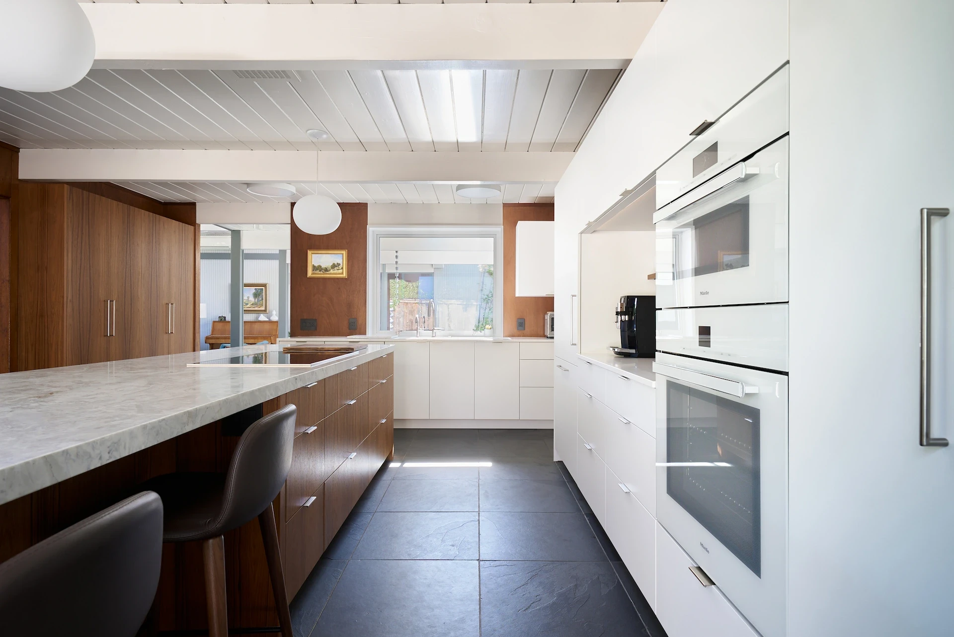 Wide view of the kitchen galley, showing the island on the left and the oven wall on the right, capturing the essence of the Eichler's modern charm. Photo by Todd Huge.