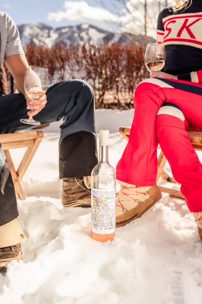 Entourage rosé bottle standing in the snow between the winter boots of two seated guests