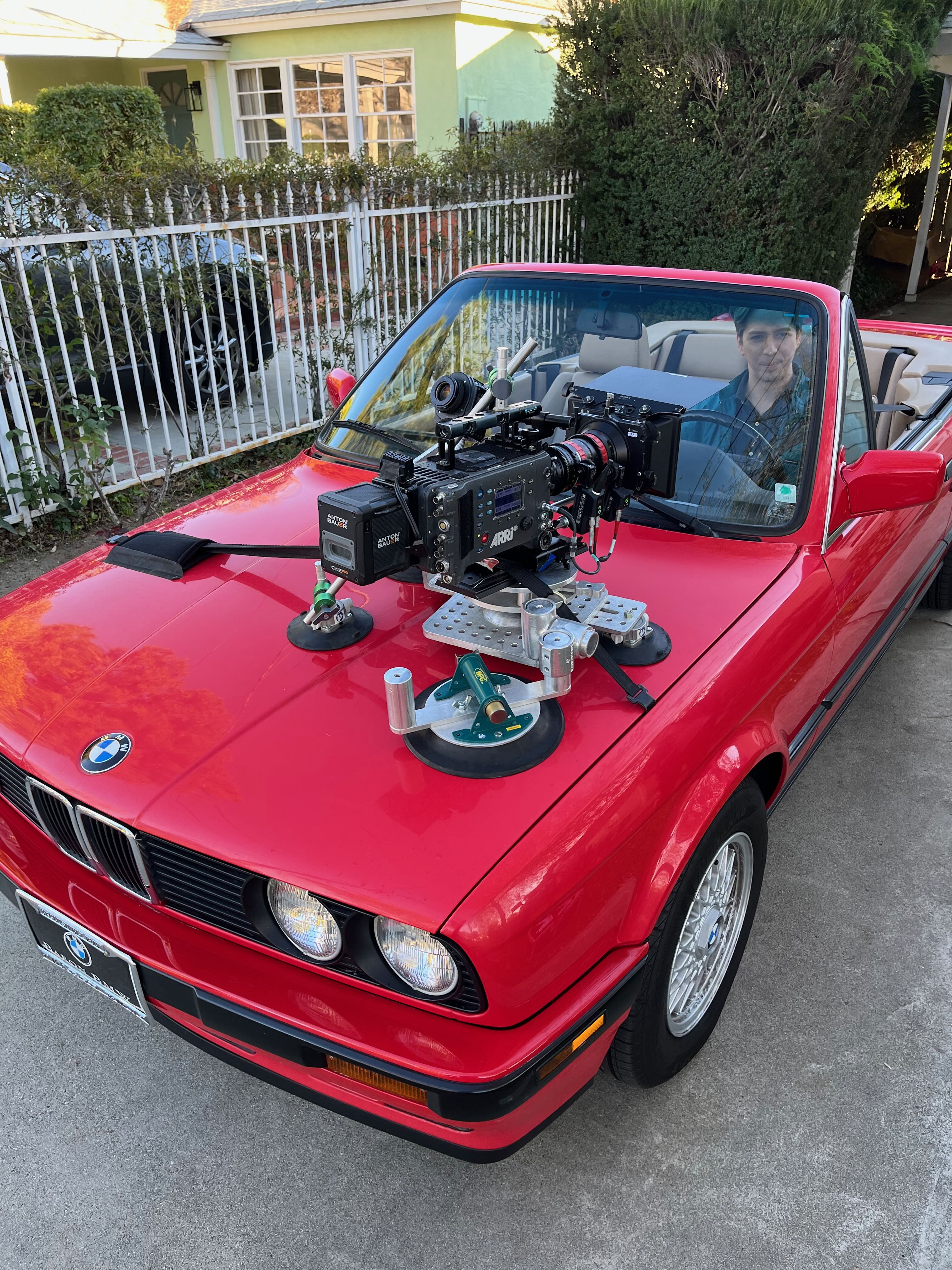Cinema camera mounted on the hood of a red convertible with suction cups and support rails