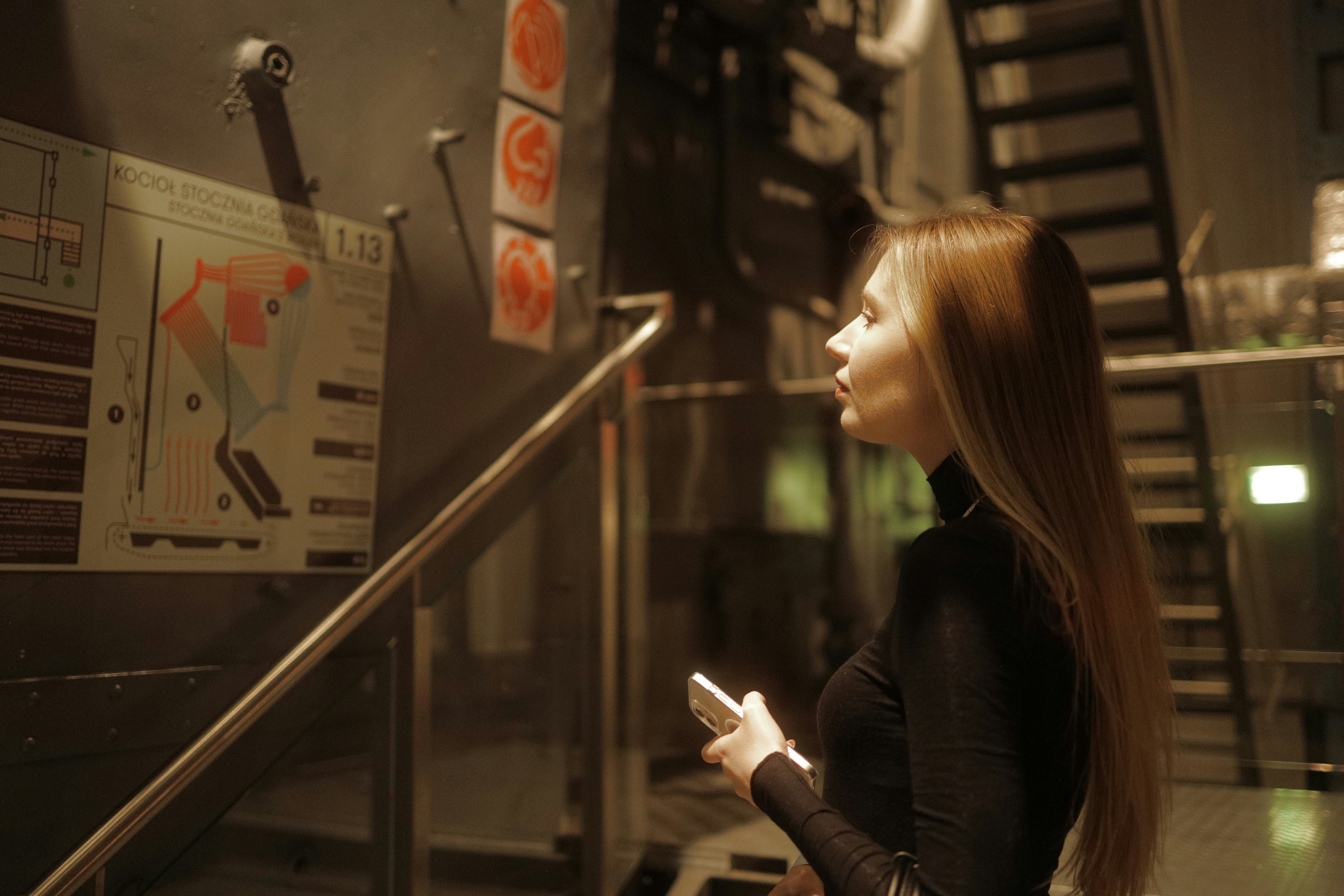 a woman standing next to a set of stairs holding a cell phone
