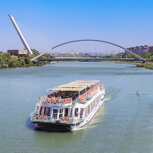 ஒரு வெள்ளை ஆற்றுப்படகு நவீன வளைந்த பாலத்துக்கீழே பயணிக்கிறது, இது நகர கட்டிடங்களும் நீல வானில் ஒரு பின்னணியும் அமைந்துள்ளது.