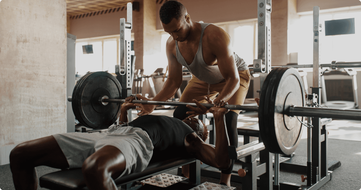 A man performing a bench press with a heavy barbell while another man spots him,