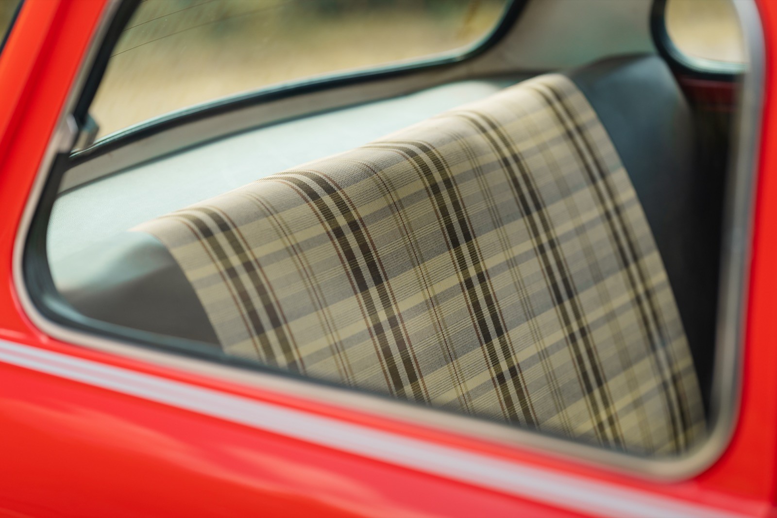 A close-up of a car window reflecting a patterned seat cover inside a red vehicle.