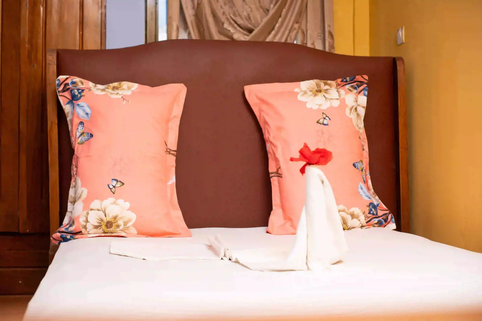 Lit double aux coussins roses à fleurs avec serviettes pliées et fleur rouge.