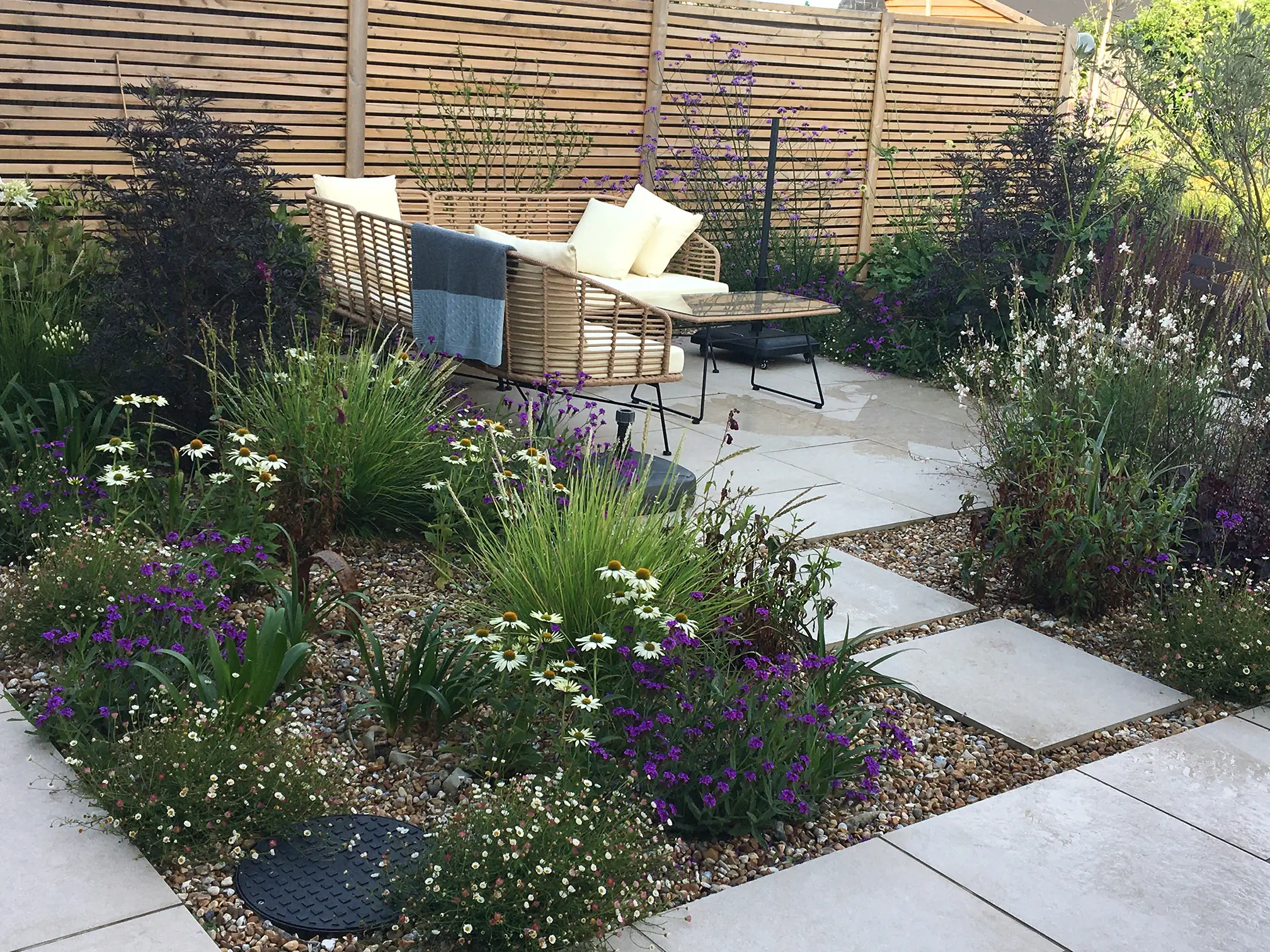 A garden with pathways, vibrant flowers, and greenery, featuring a small table and chairs in the background.