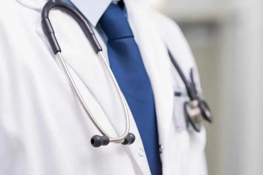 AI-driven medical coding simplified as a close-up of a doctor in a white coat and blue tie with a stethoscope draped around the neck.