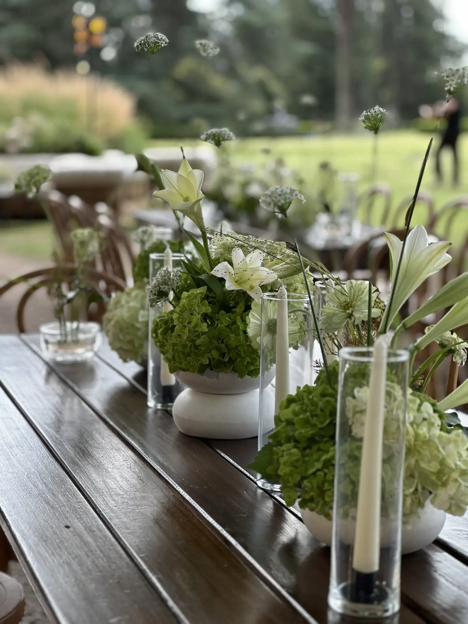 Mesa de recepción con lirios, hortensias y velas en cilindros de vidrio para eventos elegantes con inspiración botánica.