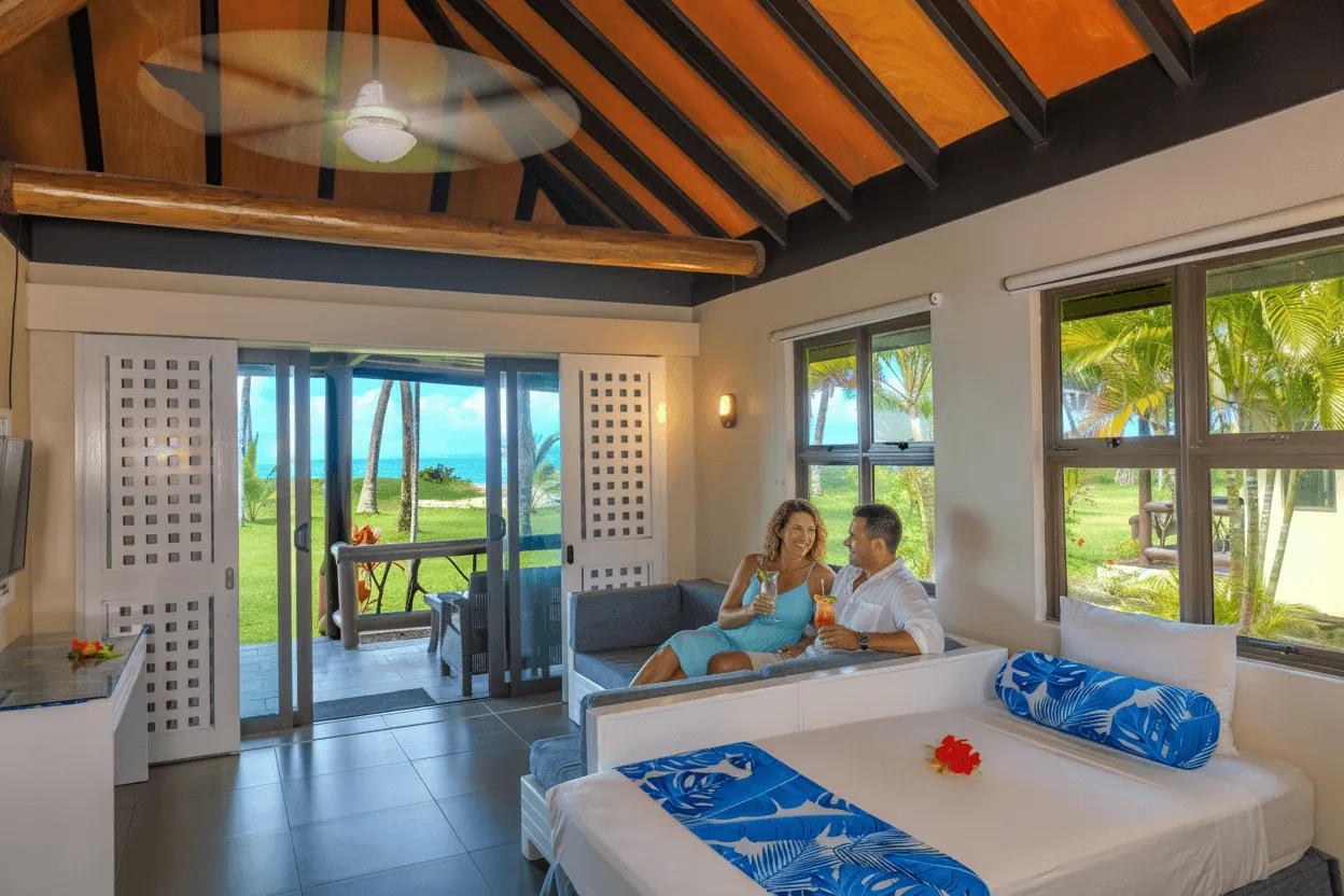 A couple enjoys cocktails in a bright beachfront bure at Uprising Beach Resort, overlooking the Fiji sea.
