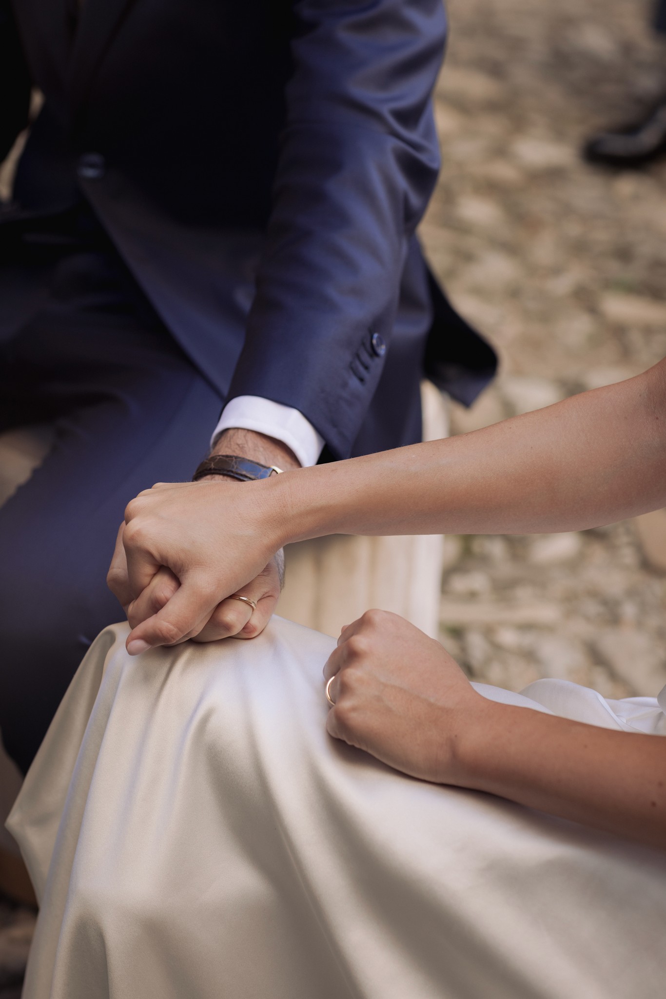 Mani degli sposi unite sull'abito bianco, dettaglio di matrimonio al Castello di Scipione con anelli nuziali in primo piano