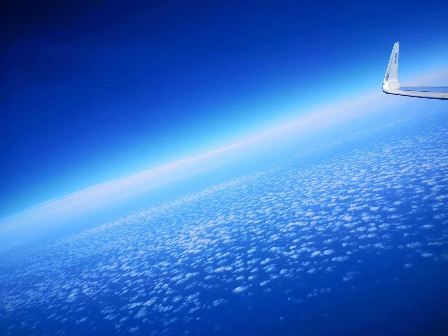 Airplane wing visible above a blanket of clouds with a vibrant blue sky