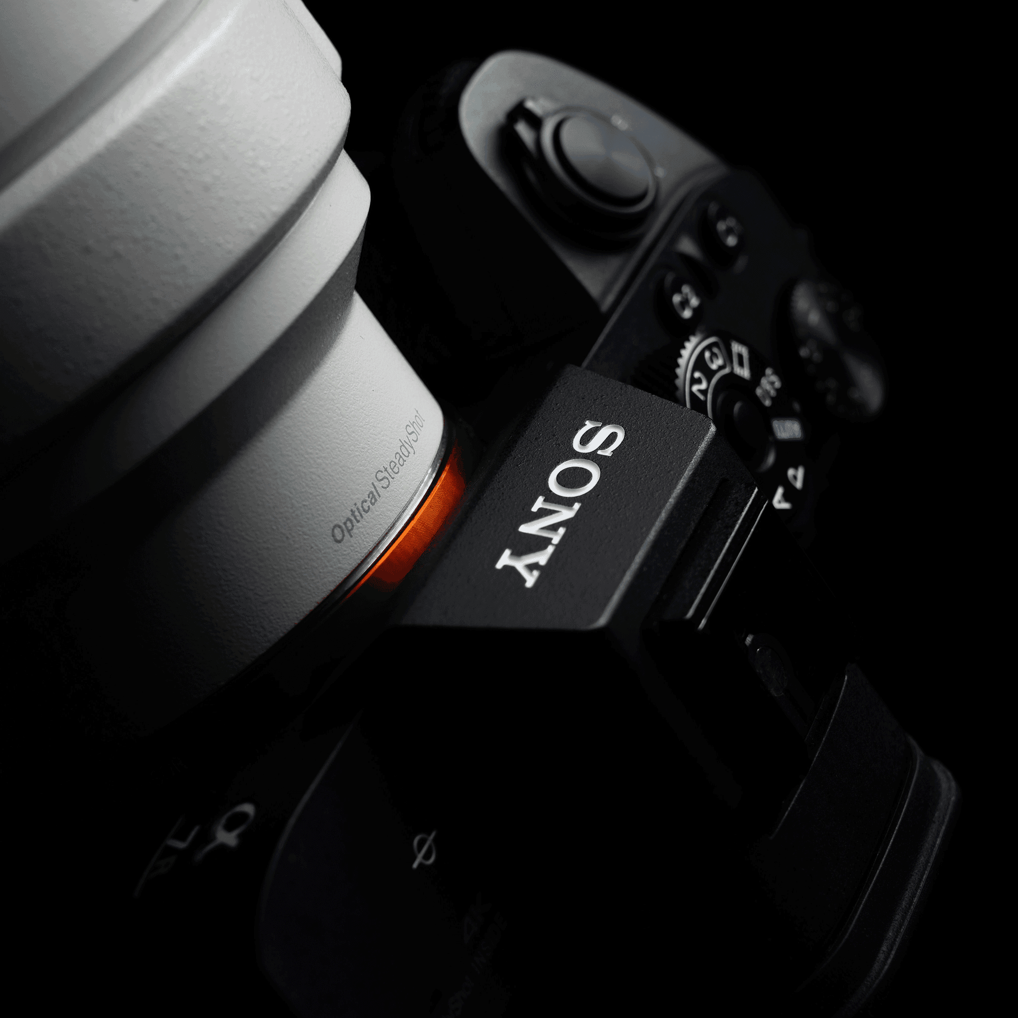 A professional digital camera with a red and black lens sits on a brick surface. It is lit with bright light.