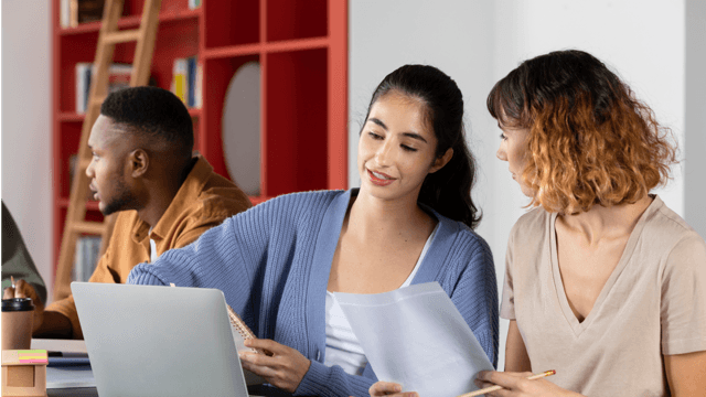 Photo of two ladies seated with one of them showing the other something on a laptop screen