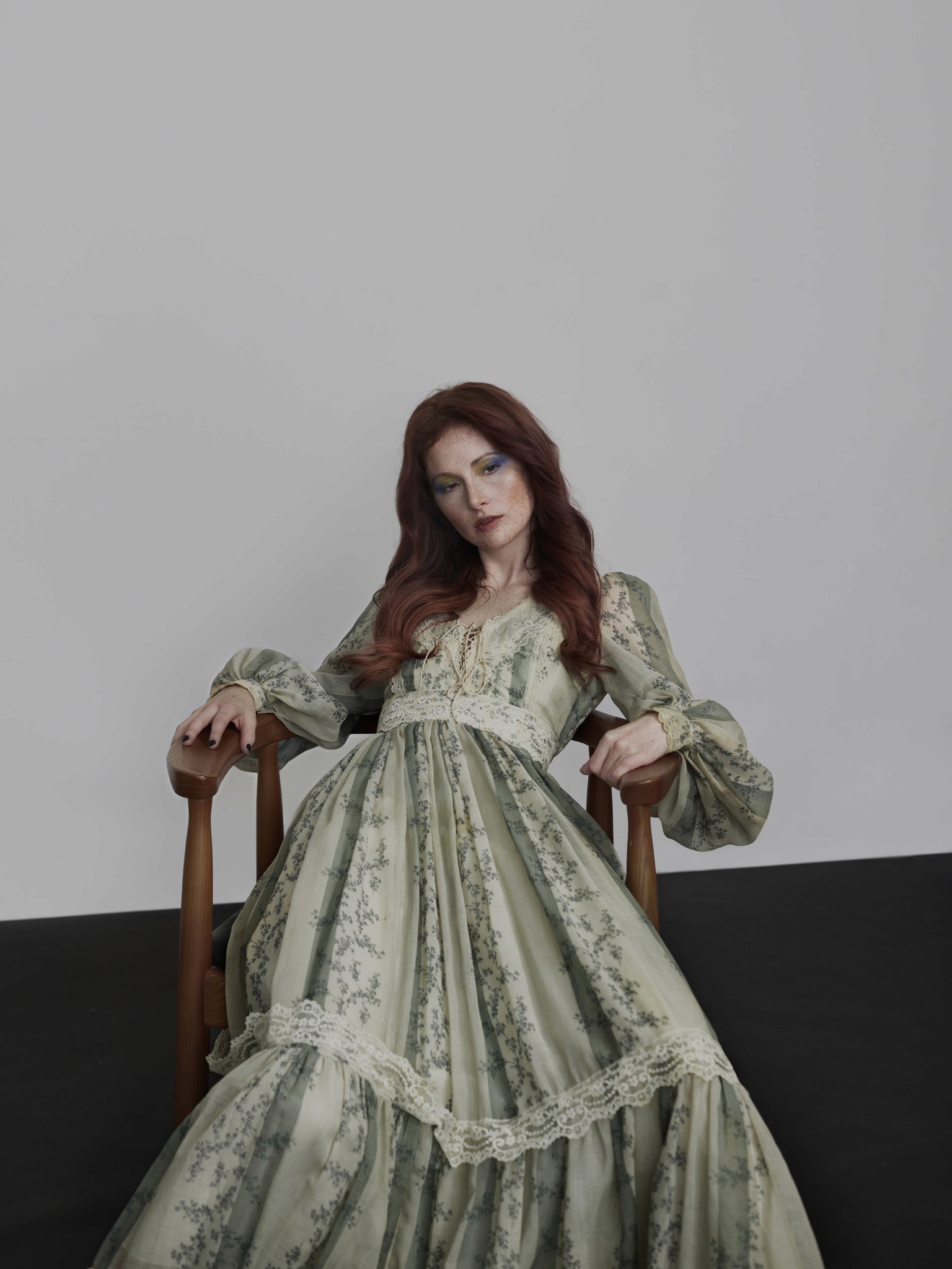 A modern graphic photographic editorial portrait of a woman sitting in a chair. She is wearing a green dress and is in an expressive pose. 