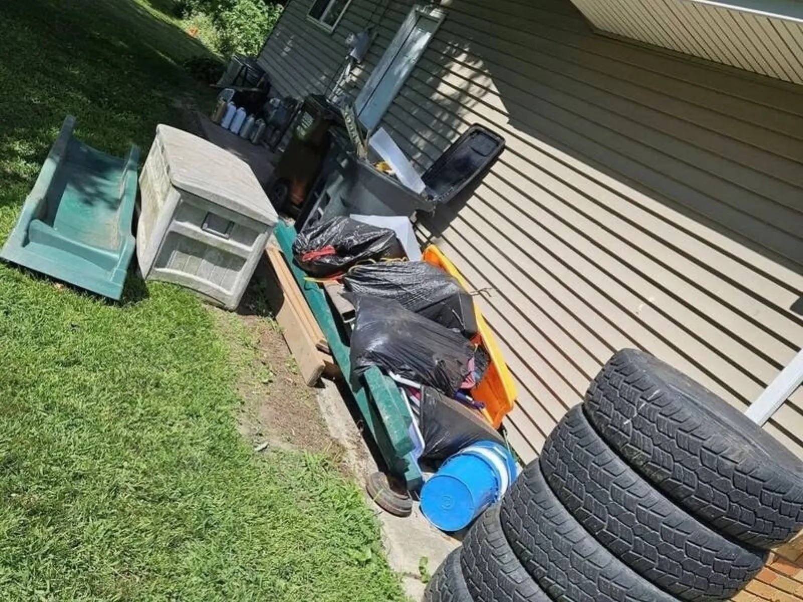 Pile of old junk, bins and a kids' slide beside a house in Temperance, MI before junk removal
