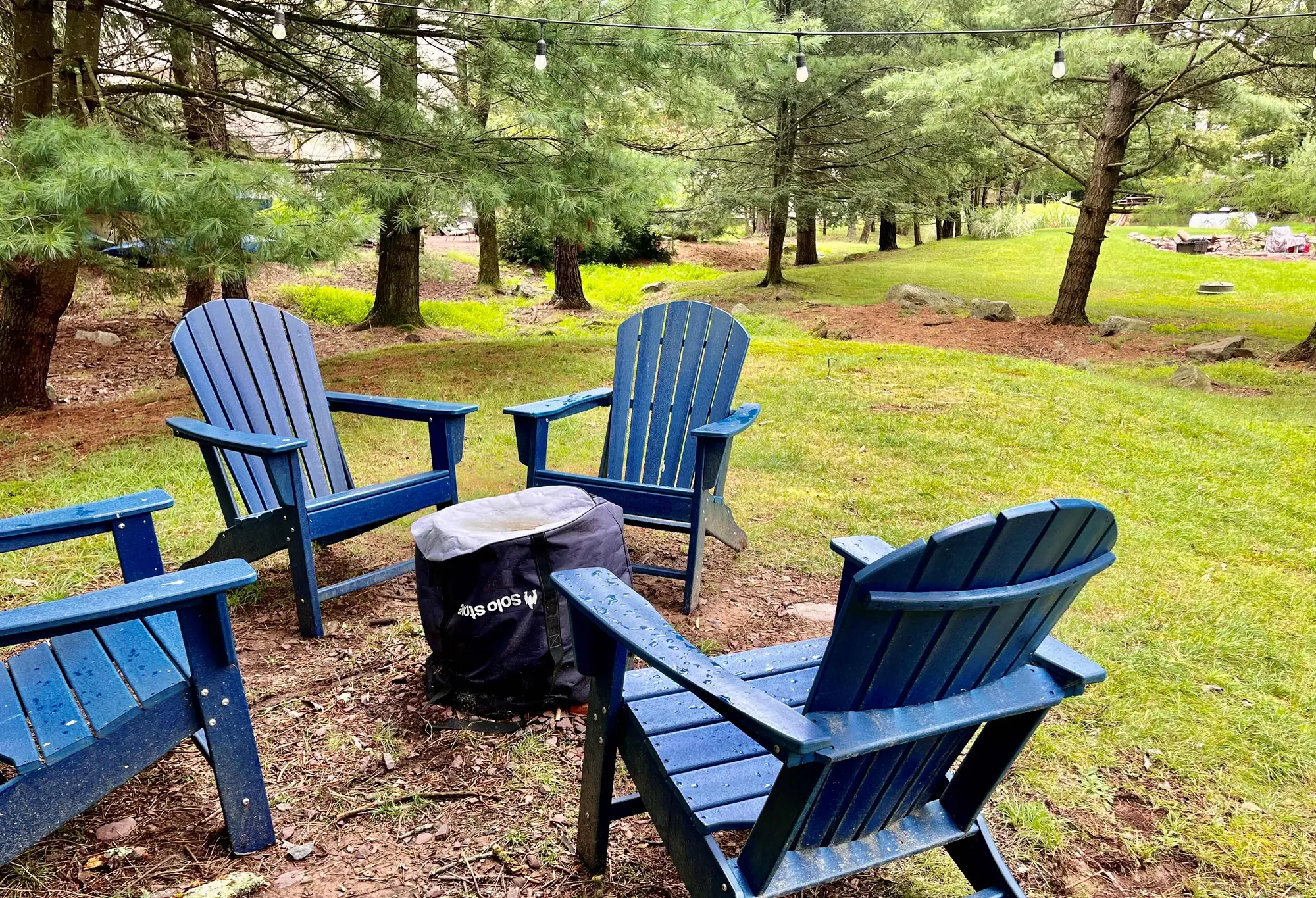 Blue Adirondack chairs around a fire pit among pine trees at Beechwood Bliss, Lake Harmony, PA