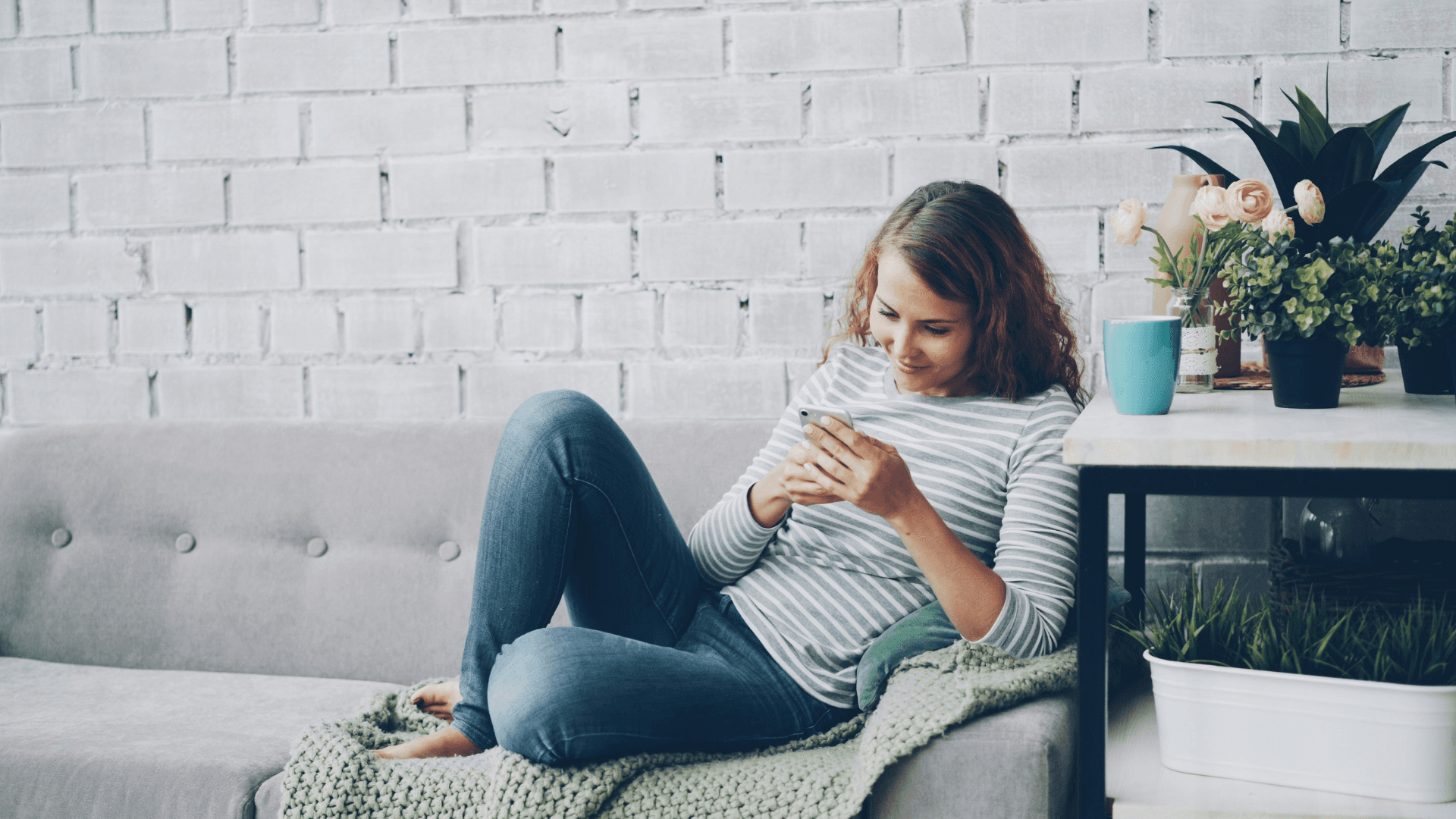 A woman sits on her couch scrolling through her mobile phone