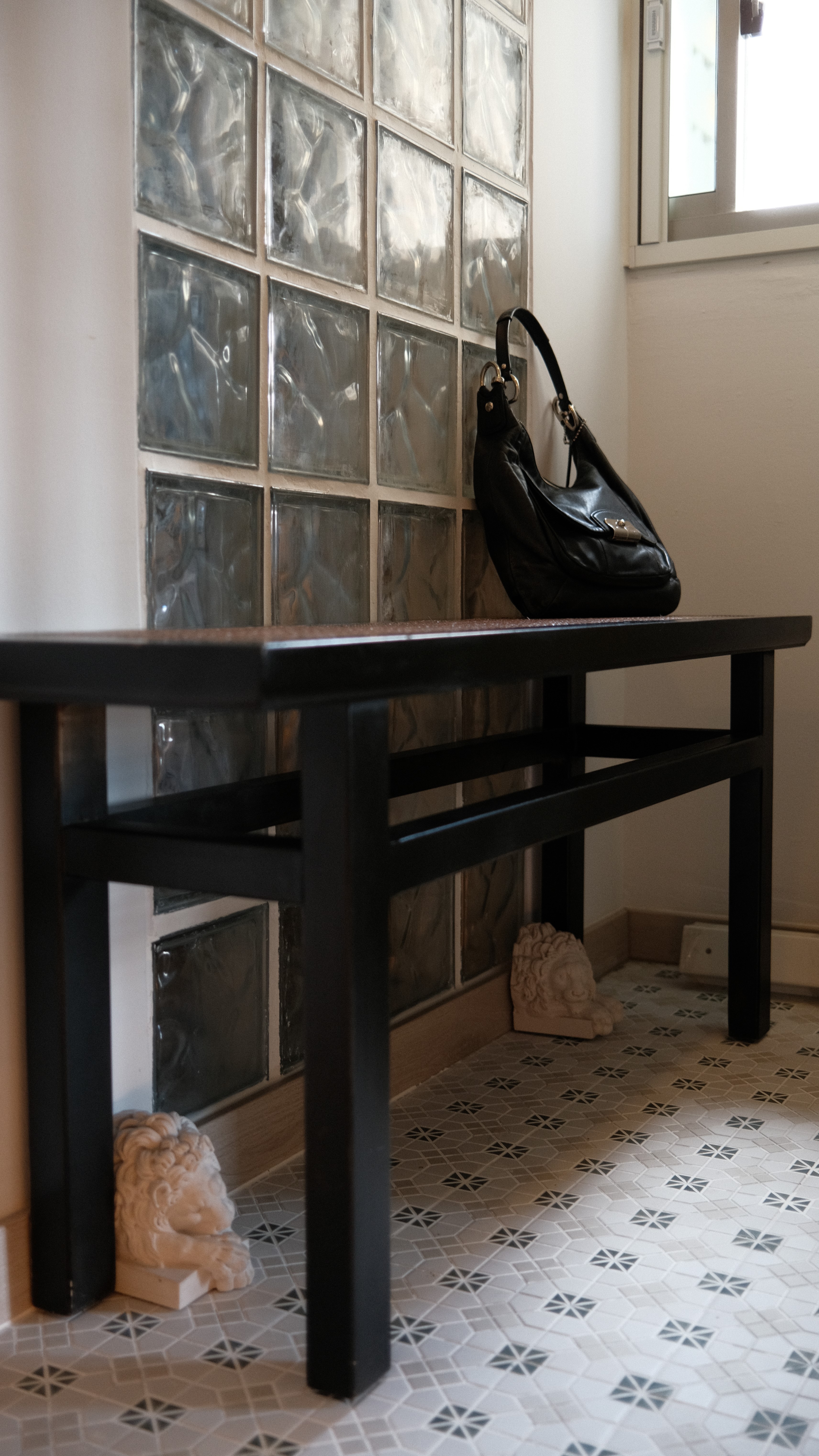 Entryway bench with black leather bag, glass block feature wall, and patterned floor tiles, highlighting the unique entrance design at Holland C.