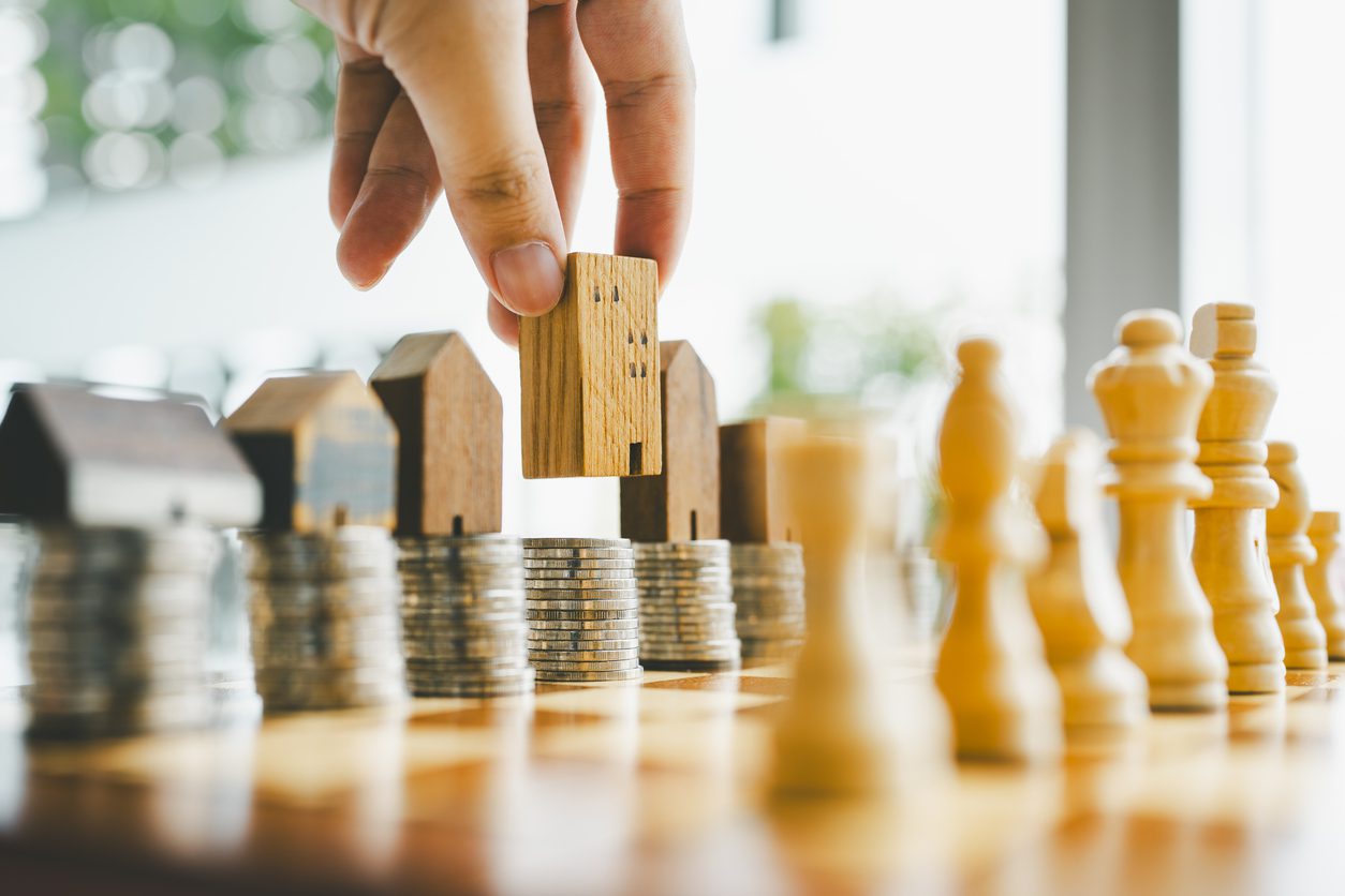 Wooden house on coins and chess pieces on board