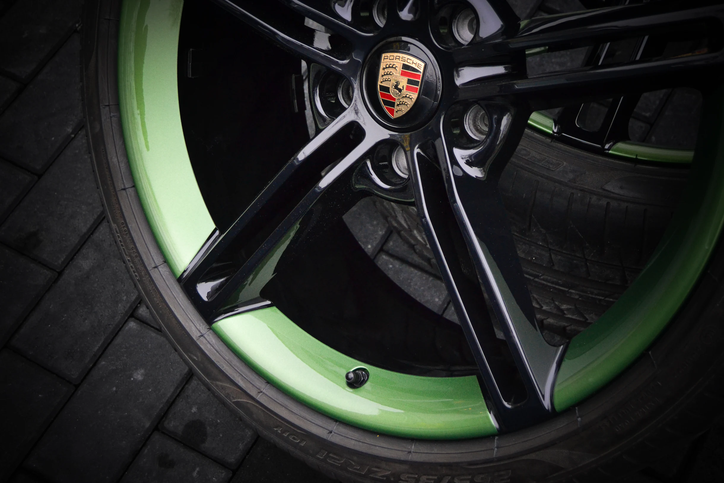 Detail der schwarzen Speichen und des grünen Felgenbetts einer Porsche-Felge bei AT Plus.