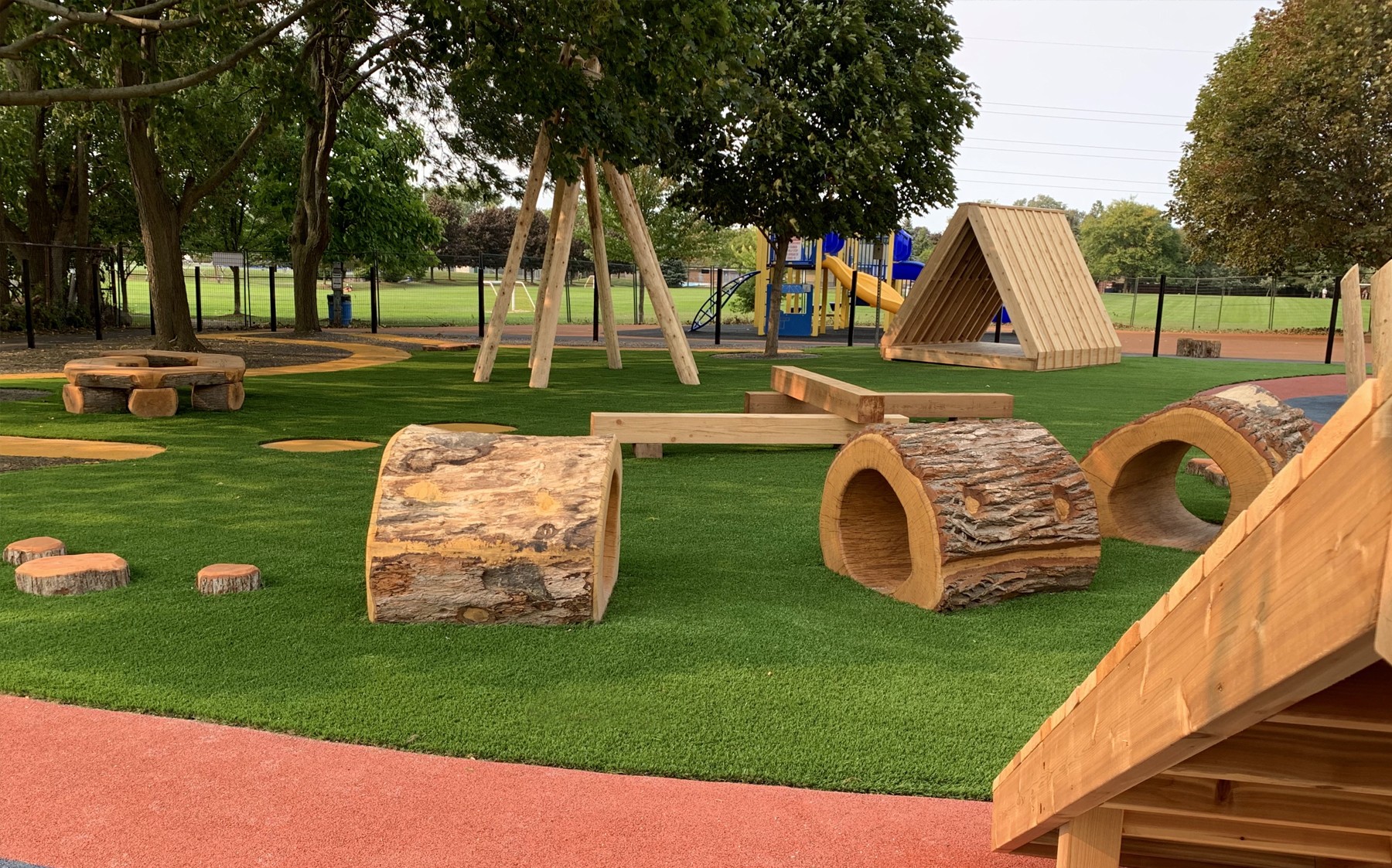 Soft, green AGL Grass found at a kid's playground with slides, a jungle gym, and wooden logs.