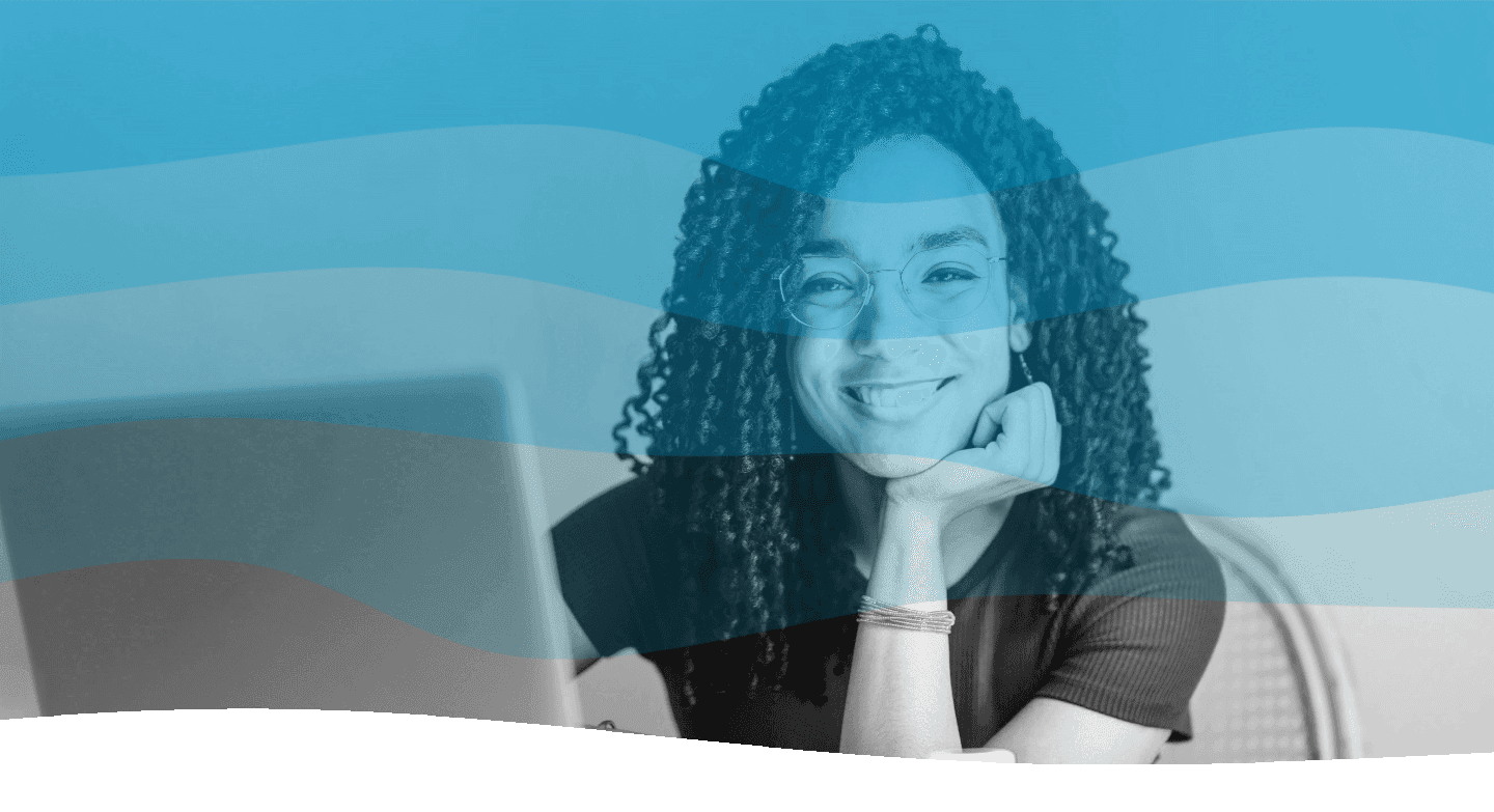 A person with curly hair, wearing glasses, is smiling and sitting at a desk with a laptop, under a wavy blue overlay.