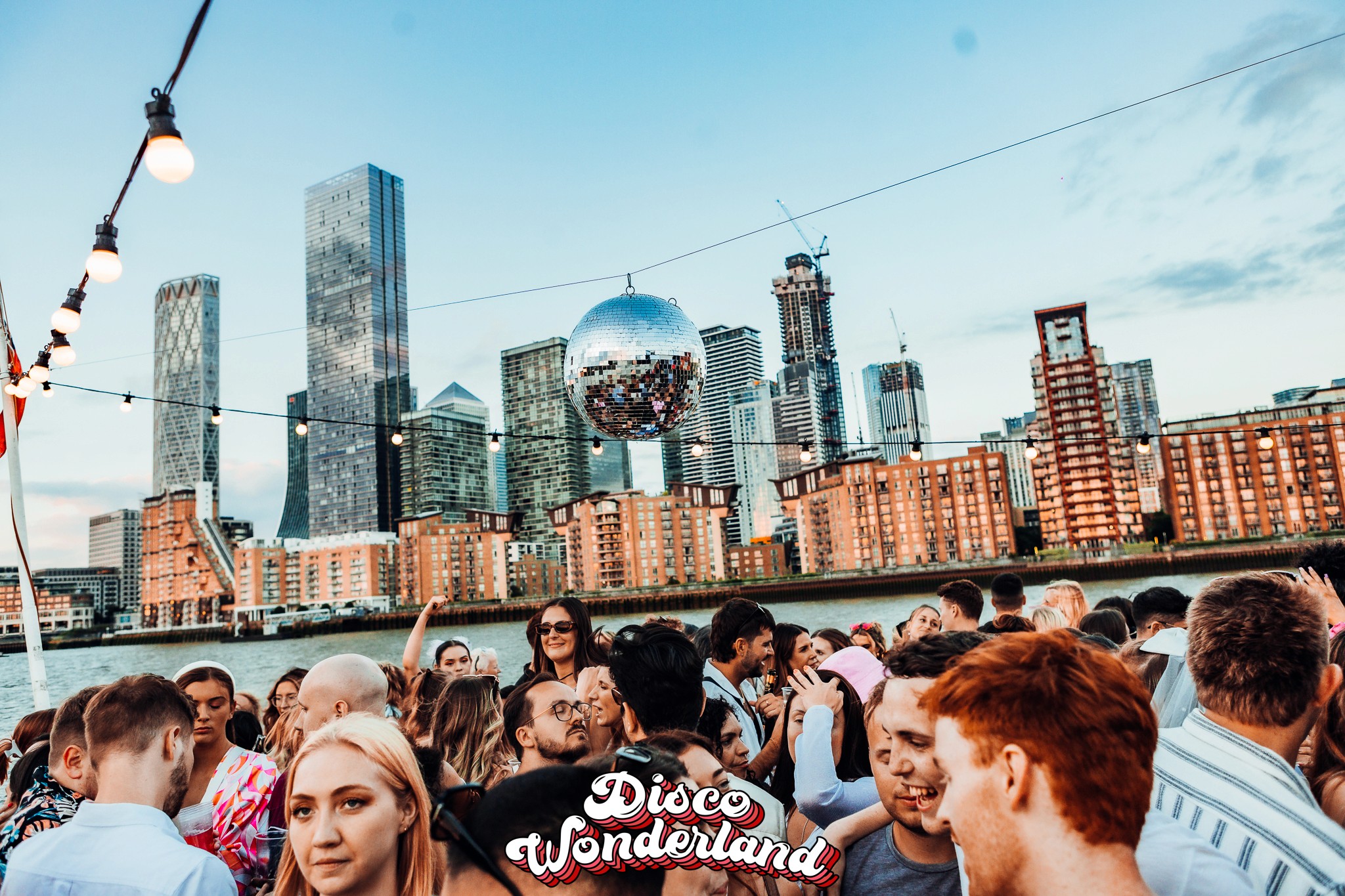 Daytime Thames boat party crowd with the London skyline in the afternoon sunshine