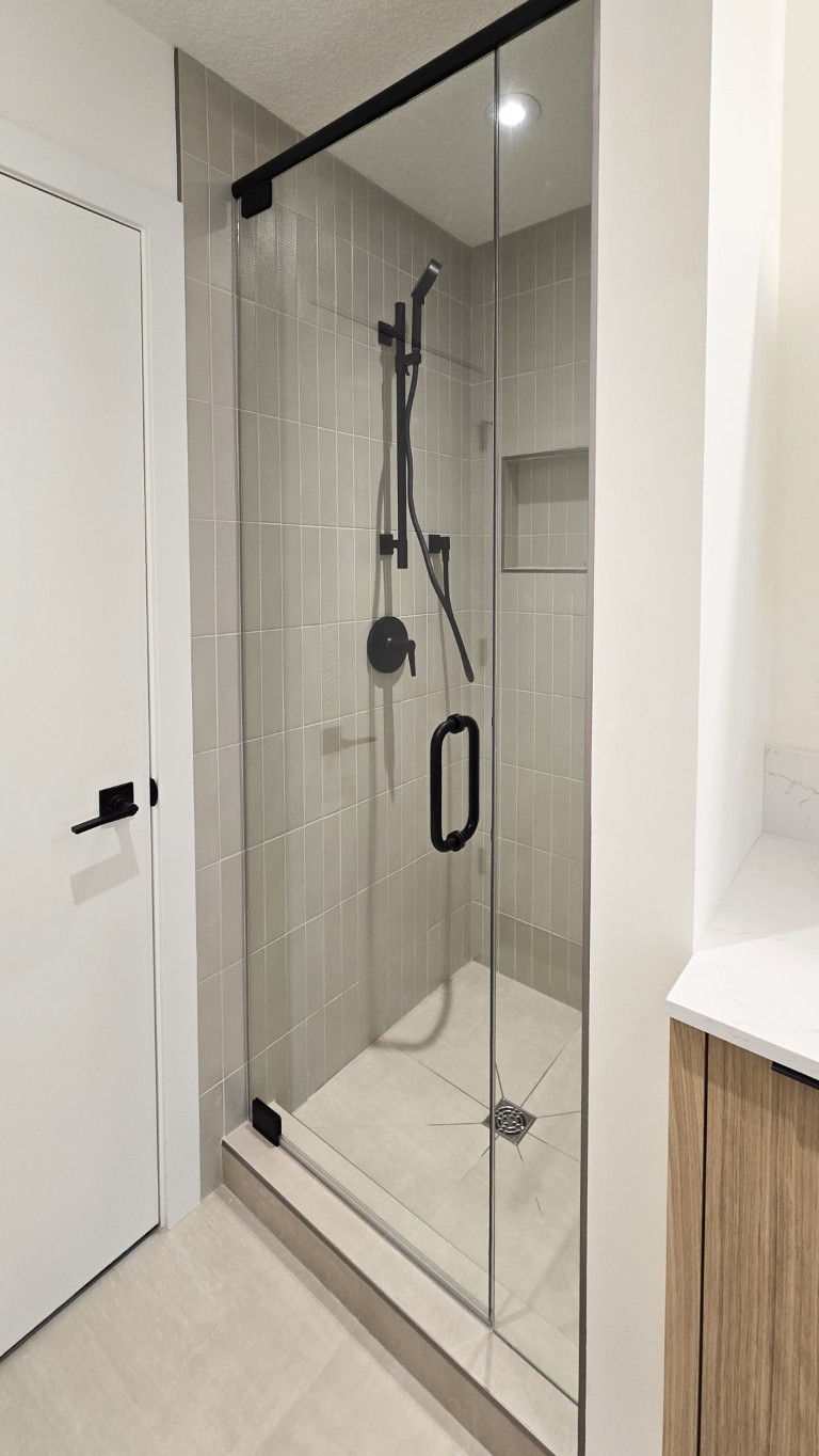 Image of Luxury primary ensuite bathroom with modern glass shower enclosure and gray tile surround by KHD Homes.