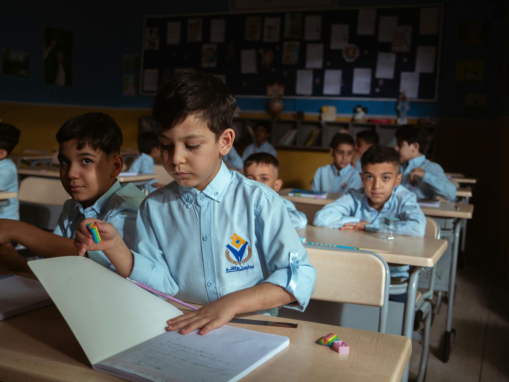 Teacher standing at a whiteboard organizing a diverse collection of leveled readers on a classroom bookshelf.
