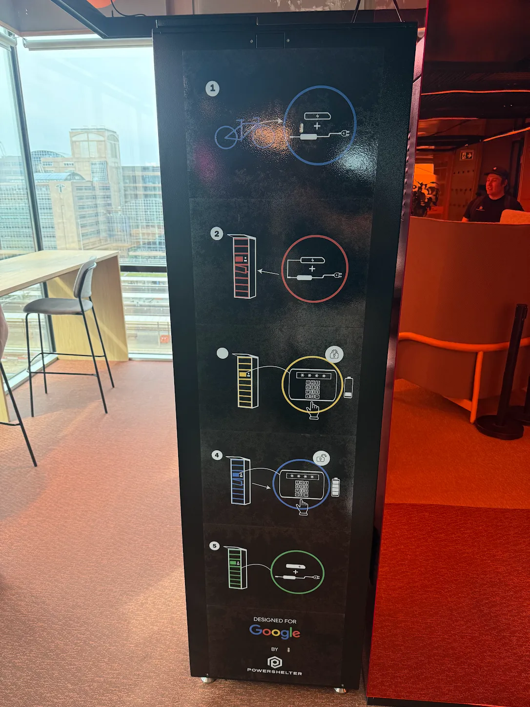 Side panel of the PowerShelter SmartShelter at Google Amsterdam, showing a five-step e-bike battery charging guide and "Designed for Google by PowerShelter" branding