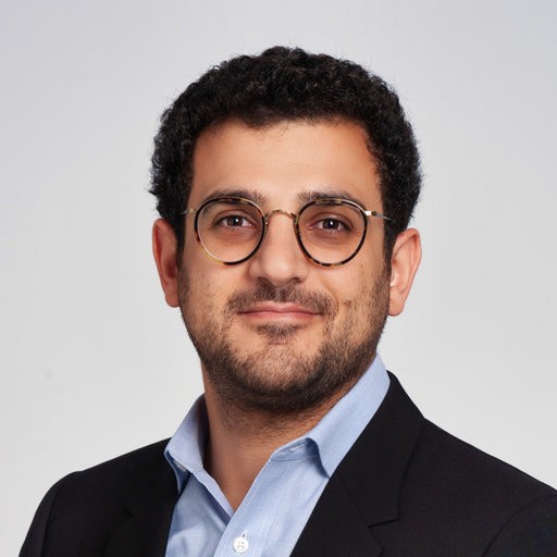 Teddy Akiki in business atire with a black coat and blue business shirt