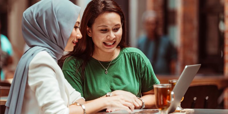 Two girls looking at a laptop in a restaurant/cafe